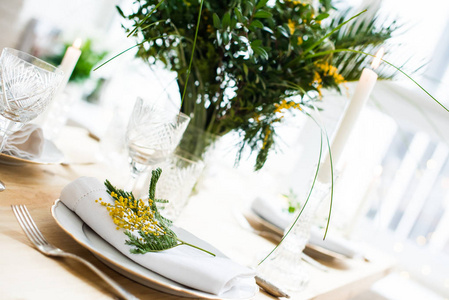 美丽的春天餐桌设置与绿叶和含羞草树枝, 明亮的白色餐桌晚餐装饰