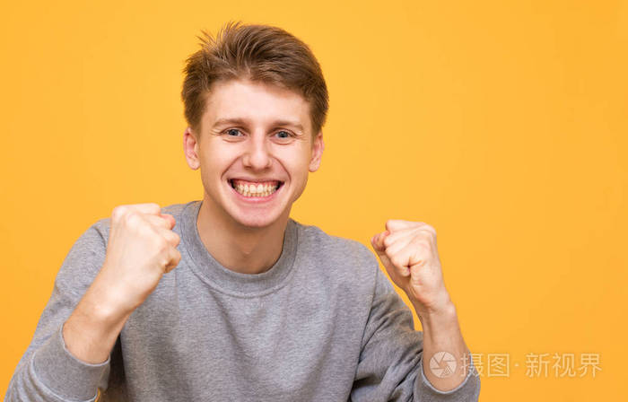 少年高兴地举起双手,看着隔离在黄色背景上的相机. 共用空间