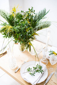 美丽的春天餐桌设置与绿叶和含羞草树枝, 明亮的白色餐桌晚餐装饰