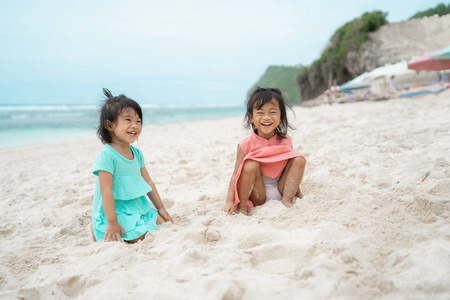 两个女儿坐在白色的沙滩上微笑