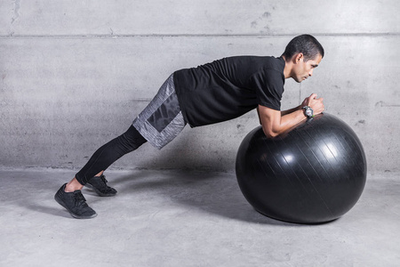 私人教练在灰色混凝土背景下用健身球展示腹肌锻炼的侧面视图