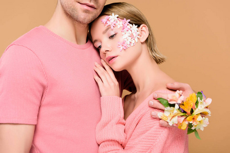 男人拥抱迷人的女朋友，脸上的花被隔离在米色上
