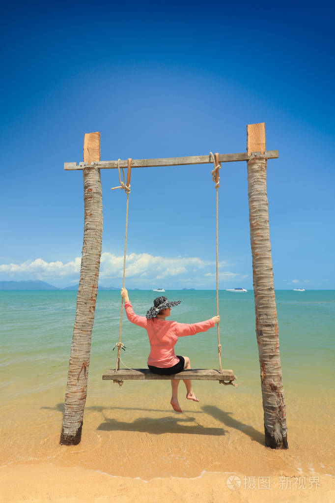 女人坐在沙滩上荡秋千,背景是阳光明媚的海景.