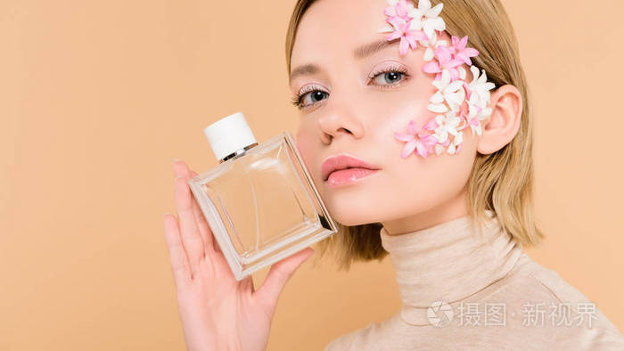 自信的女人脸上有花手里拿着一瓶香水隔离在米色上