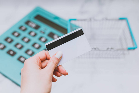 s hand holding payment card in front of huge calculator and shop