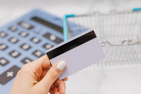 s hand holding payment card in front of huge calculator and shop