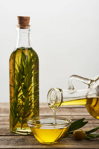 将橄榄油从瓶中倒入装有迷迭香橄榄树叶和橄榄的玻璃瓶中