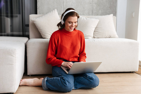 快乐的年轻，随便打扮的女人，坐在地板上，在家里用笔记本电脑学习