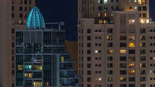 在多层现代玻璃住宅建筑中发光的窗户在夜间时间推移时亮起。 公寓里的人。 摩天大楼在晚上照明。 迪拜码头和JBR阿联酋。