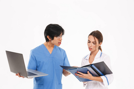 严肃的医生夫妇穿着制服站在白色背景上，用笔记本电脑和x射线照片工作