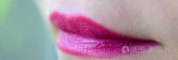 特写美丽的女人嘴唇与光泽的紫红色口红。 浅场深
