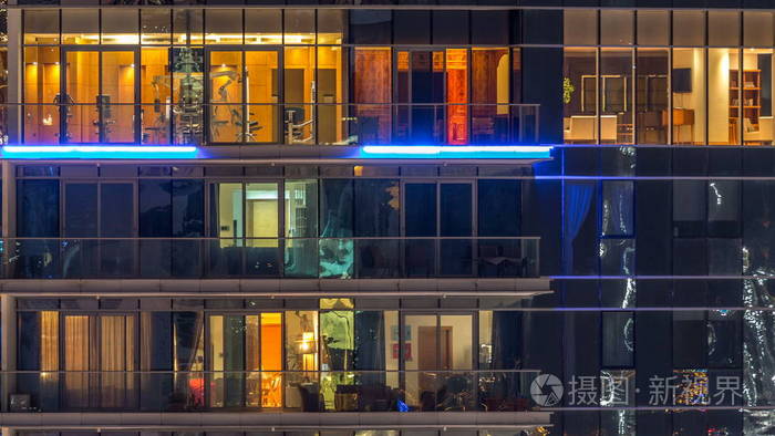 在多层现代玻璃和金属住宅建筑中发光的窗户在夜间延时亮起.
