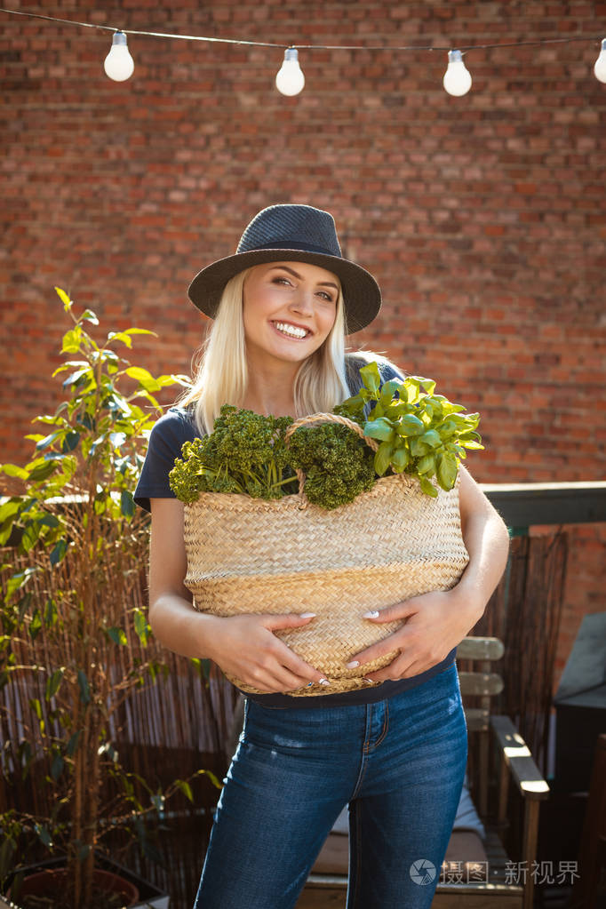 户外拍摄的美丽的年轻女子拿着篮子和甘蓝和绿色蔬菜. 对着镜头微笑.