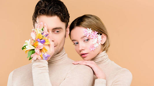一个男人，手上拿着一朵花，遮住一只眼睛，靠近漂亮的女朋友，脸上拿着花，米色的，孤立的