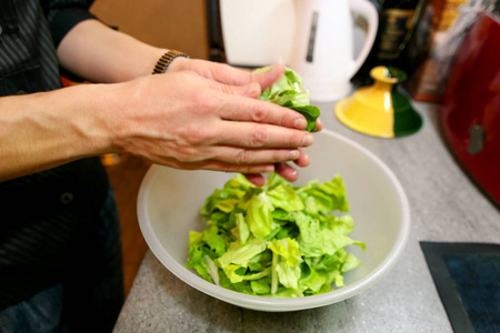 闭上女性的手，女人在厨房准备绿色沙拉烹饪。 家庭主妇切片和准备新鲜沙拉。 厨师在塑料碗里切青菜。 素食和健康的烹饪理念。