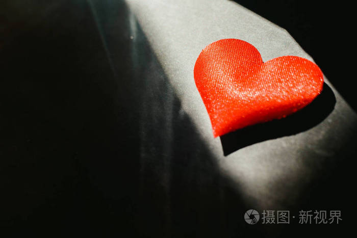 红心孤立的黑暗背景被一缕阳光照亮在背景中使用大量的空白复制空间