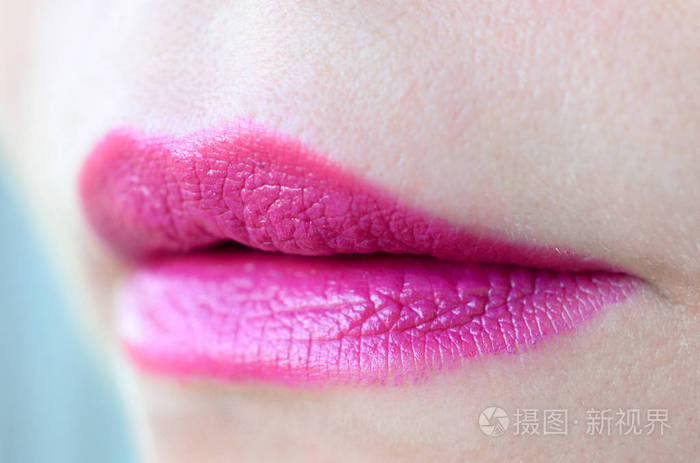 特写美丽的女人嘴唇与光泽的紫红色口红。 浅场深