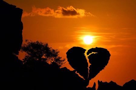 破碎的心形石头在一座有红色天空日落背景的山上.