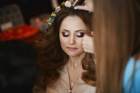 化妆师应用明亮的婚礼化妆与时尚的婚礼发型美丽的黑发模型女孩, 年轻新娘的婚礼准备