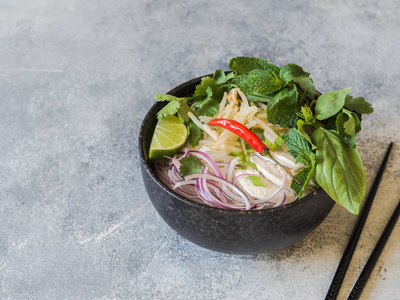 传统越南汤PHOGA在黑碗与鸡肉和米粉薄荷和香菜青红洋葱辣椒豆芽和石灰在灰色背景。