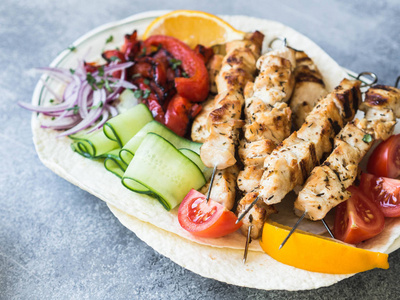 烤鸡在金属串上，新鲜蔬菜在皮塔和希腊酱汁在一个灰色背景的碗。 希腊美食。