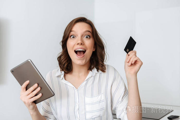 快乐的年轻女商人坐在家里的厨房里，用平板电脑，拿着信用卡