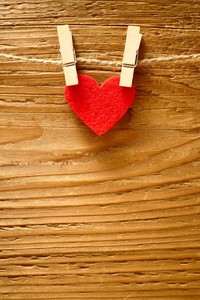一颗红色的心挂在绳子上，两个别针在棕色的木栅栏背景前。情人节快乐。