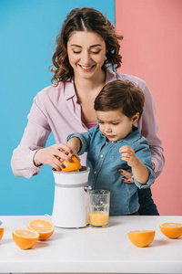 快乐的母亲和可爱的儿子一起挤压新鲜橙汁，双色背景