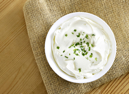 奶油奶酪夸克或酸奶在一个白色的碗。 乳制品与新鲜草药健康饮食主题。 木制桌子背景。