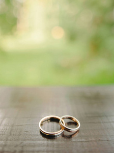 金色结婚戒指的木制表面绿色背景与复制空间