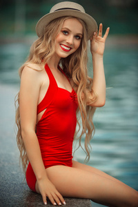 漂亮的女孩穿着红色的泳衣, 靠蓝色的水在游泳池附近休息。暑假