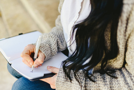 s hand taking notes in her notebook with pen, sitting.