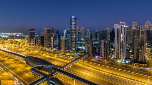 迪拜码头摩天大楼日出前从JLT在迪拜夜间到白天从阿联酋。 照亮了谢赫扎耶德路上的现代塔楼和交通。