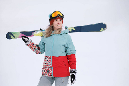 一个穿着极限运动服帽子和带口罩的头盔的美丽的年轻咀嚼在冬季山坡上举行着高山滑雪板