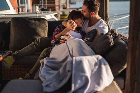 男人亲吻他微笑的女朋友的额头,而她被河边的毯子覆盖照片