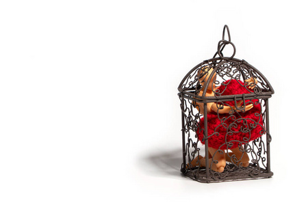 动作人物坐在笼子里，在白色背景上抱着红色的心。 爱和监禁的概念