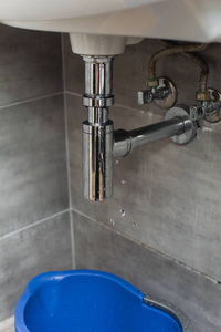 蓝色水桶站在浴室漏水的管子下面