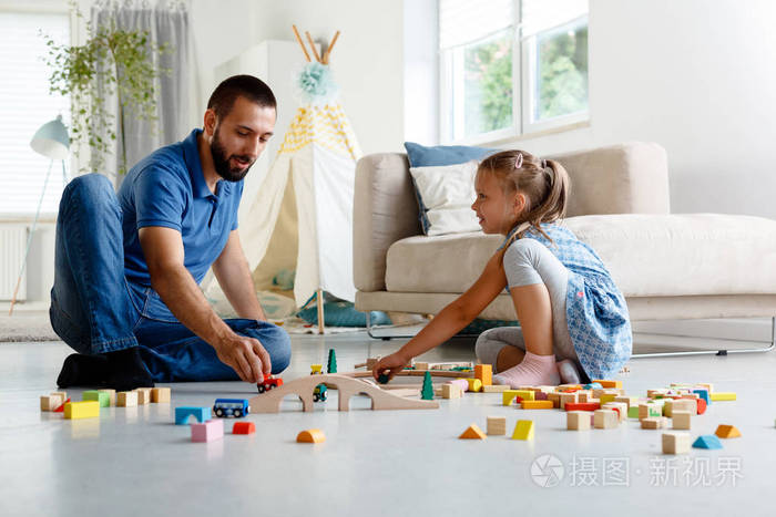 父亲和他的女儿一起在家玩积木,坐在客厅的地板上.