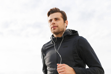 穿黑色运动服和耳机在海边锻炼和跑步的30岁运动员的形象