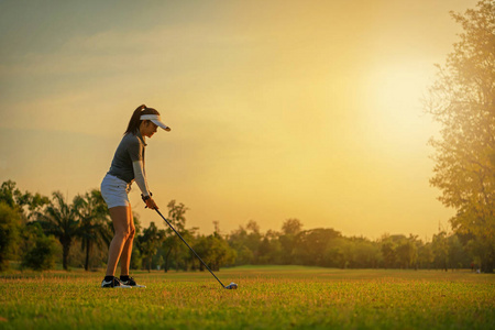 健康运动。 亚洲运动的女人高尔夫球手在绿色的日落傍晚打高尔夫球，她大概会做运动。 健康和生活方式概念