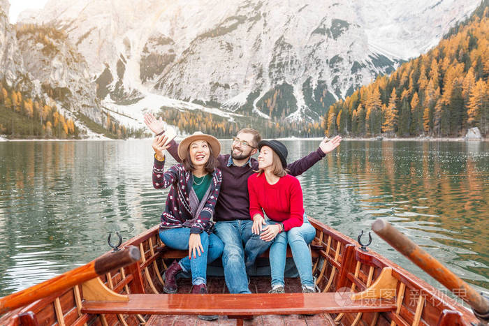 一群三个快乐的旅行者坐在山上一个湖上的木船上。 意大利白云石的度假和旅游概念