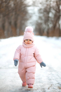 一个美丽的年轻女孩穿着粉红色的连体衣在一个下雪的冬天公园里跑步。 小孩在雪地森林里玩耍和跳跃