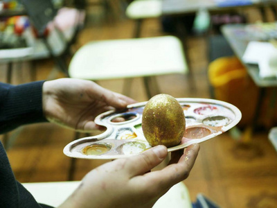 学生手里拿着一个调色板，上面画着一个复活节彩蛋，一个背景调色板，一个艺术学校为复活节做准备的工作坊