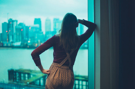 一个年轻的女人在一个城市的公寓里，正在看外面的摩天大楼