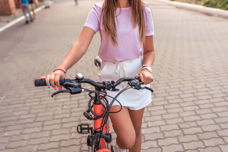 夏天, 一个女孩拿着自行车站在城里。特写方向盘和刹车, 框架上有一个安全秘密锁。休闲装的妇女