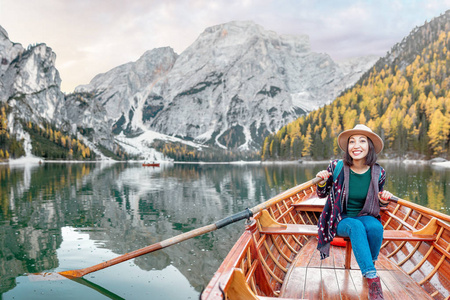 快乐的亚洲女人坐在木制的老式船上，漂浮在意大利阿尔卑斯山脉的布莱斯湖上，旅行和梦想的度假理念