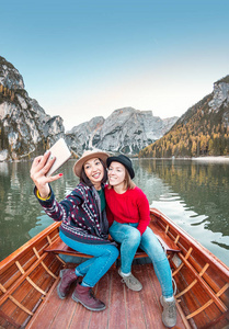 两位快乐的女性朋友在意大利多洛米斯阿尔卑斯山的拉戈迪布赖斯湖上小船或独木舟游船上自拍。