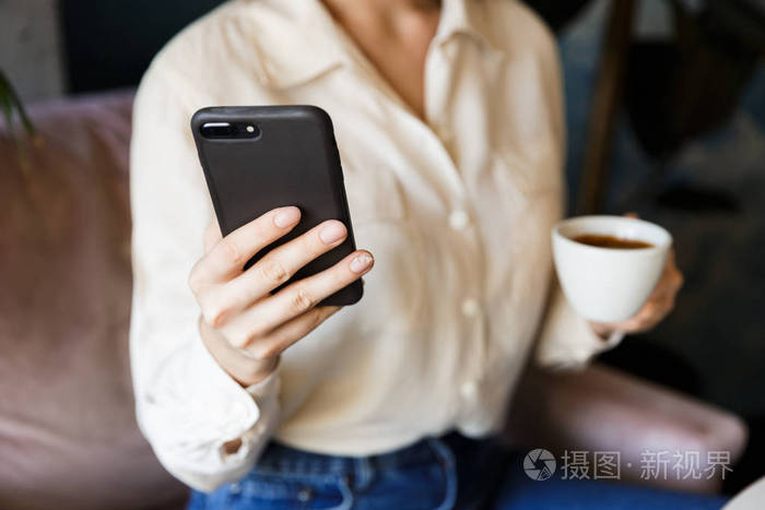 一个美丽的年轻女人坐在咖啡馆里,在室内工作,用手机喝咖啡.