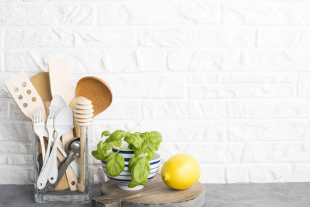 厨房工具，厨房架子上的橄榄切割板靠在白色砖墙上..有选择的焦点。新鲜罗勒和柠檬。白色和黑色的现代餐具。没有塑料房子