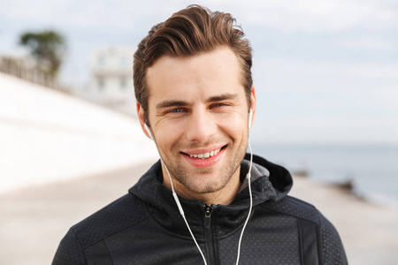 运动男30岁左右，穿黑色运动服，在海边散步时使用耳机和手机
